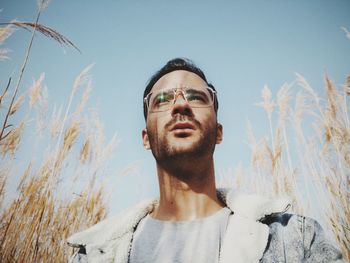 Young man wearing eyeglasses while standing by plants against sky