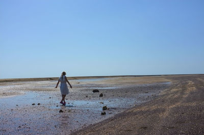 Rear view of man walking on beach against clear sky