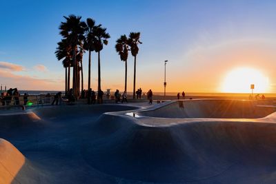 People by skateboard park and sea against sky during sunset