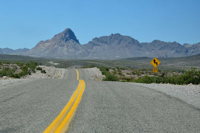 Yellow road by mountains against clear sky