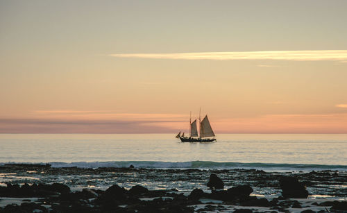 Sailboat sailing on sea against sky during sunset