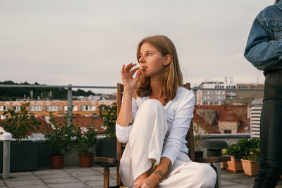Young woman sitting outdoors against sky