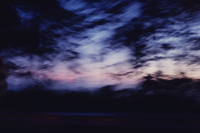 Defocused image of silhouette trees against sky at sunset
