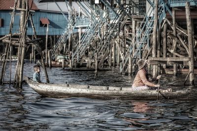 Side view of woman rowing canoe while sitting with boys on river