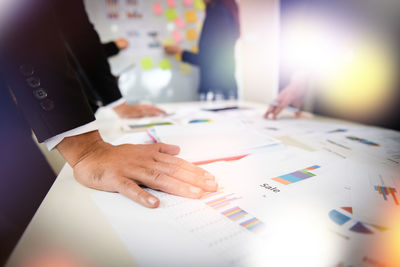 Man standing by graphs on table while colleagues discussing in background