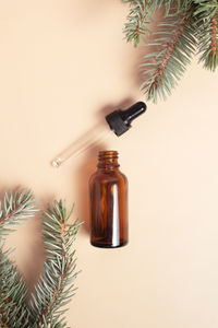 Flat lay of facial oil amber bottle and fir tidewater green branches, cosmetic products on beige