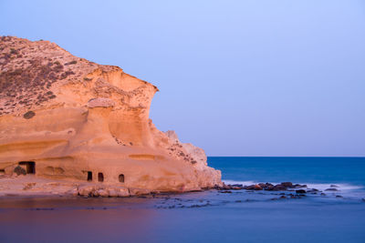 Rock formations in sea against clear blue sky