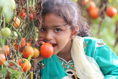 Portrait of girl holding fruits by plant outdoors