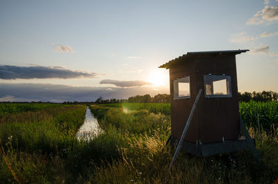 Cabin of hunter on agricultural field with small river in countryside of germany during sunset