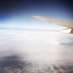 Airplane wing over landscape against blue sky