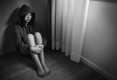 Unhappy lonely teen girl sitting in a room on the floor