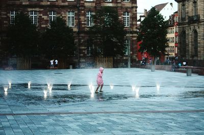 Child enjoying in water fountain against buildings