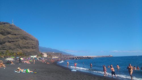 People on beach against clear blue sky