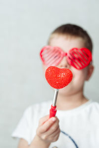 Portrait of a smiling boy in heart-shaped glasses in a white t-shirt against a white background