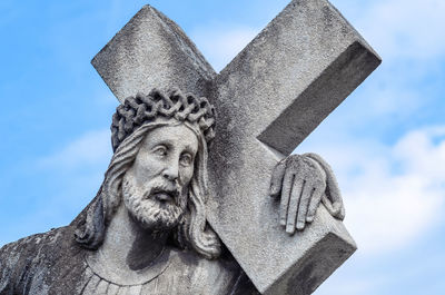Statue of jesus on tombstone, carrying a cross against a blue sky background