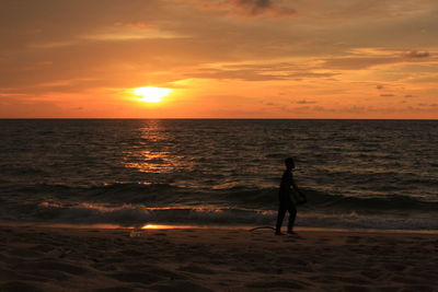 Silhouette man standing on beach against sky during sunset