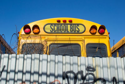 School bus by corrugated iron against clear blue sky