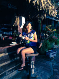Young woman sitting on stool while having coffee outside cafe