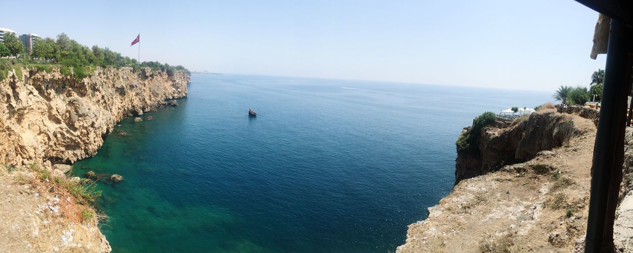 sea, water, horizon over water, clear sky, beach, tranquil scene, scenics, tranquility, beauty in nature, shore, nature, incidental people, blue, copy space, coastline, cliff, sand, vacations, rock - object, tree