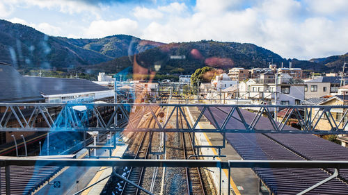 Man reflecting on glass window while photographing railroad station against mountains