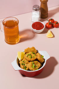 Crispy nuggets in a plate and ketchup on a pink background with hard shadows.