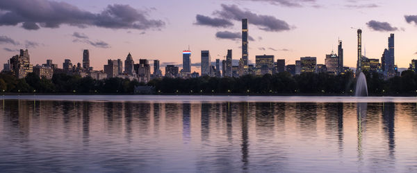 Scenic view of lake by buildings against sky during sunset