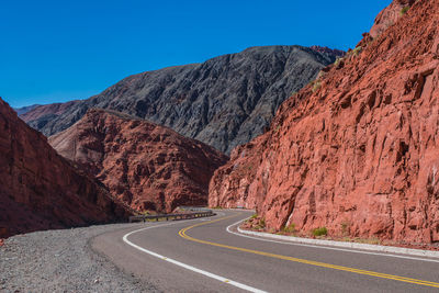 Road leading towards rocky mountains against clear sky