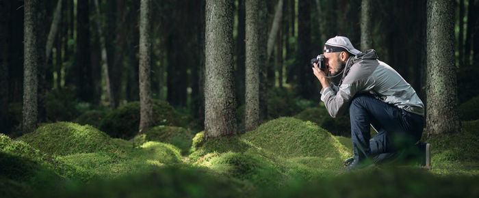 Man photographing by tree trunk in forest