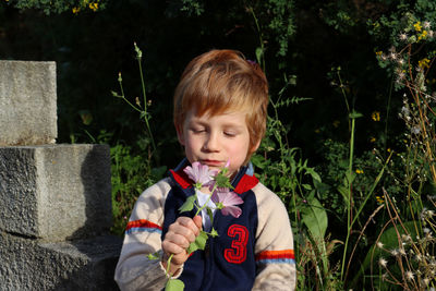 The red-haired boy smiles and looks at the flowers in his hand.