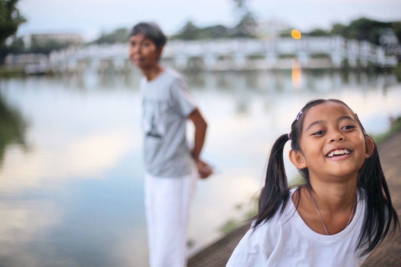 two people, real people, water, childhood, focus on foreground, casual clothing, lifestyles, emotion, lake, females, girls, smiling, leisure activity, women, happiness, day, child, outdoors, hairstyle, daughter