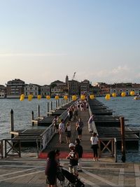 People on pier by river against sky