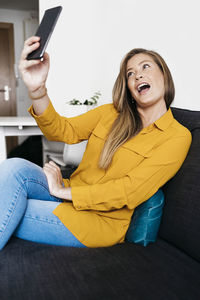 Young woman taking selfie with mobile phone while sitting on sofa at home