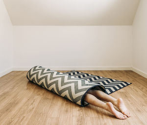 Person with bare feet rolled up inside carpet on floor in empty room