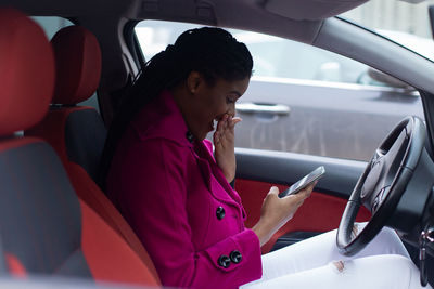 Smiling woman using smart phone while sitting at car