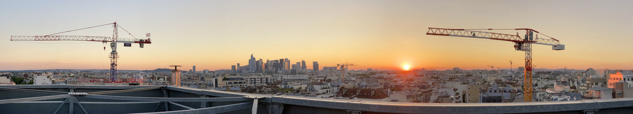 Cranes in city against sky during sunset