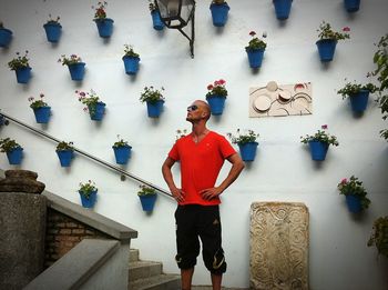 Young man with hands on hip while standing on steps against potted plants on wall