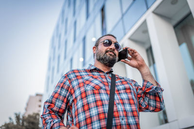 Portrait of handsome businessman with sunglasses and plaid shirt walking in the street
