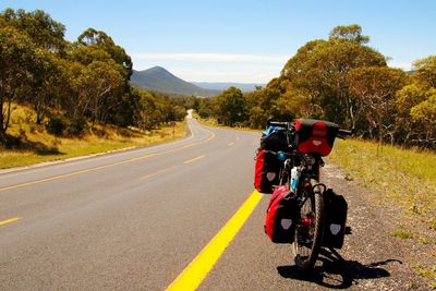 Bicycle with luggage bags parked by road against sky