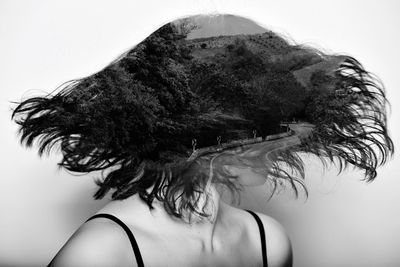Double exposure of woman tossing short hair and mountain road amidst trees against gray background