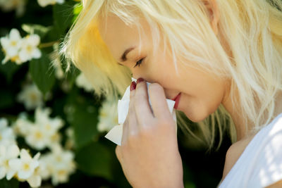 Close-up of teenage girl blowing nose in tissue outdoors