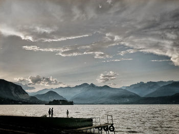 Silhouette people standing by lake against sky