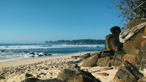 Rear view of people on rocks at beach against clear blue sky