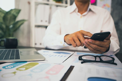 Midsection of man using smart phone on table