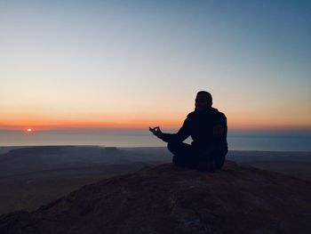 Silhouette man sitting on rock against sea during sunset