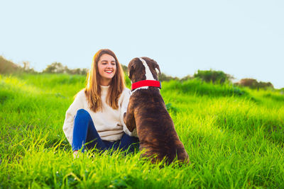 Full length of woman sitting on grass with dog outdoors