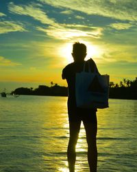 Rear view of silhouette man standing by sea against sky during sunset