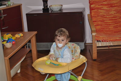 Portrait of cute baby boy sucking pacifier in walker at home
