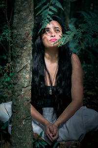 Thoughtful beautiful woman sitting on land in forest