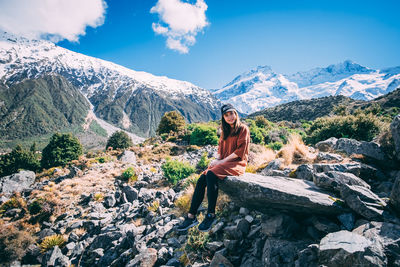 Portrait of young woman sitting on rock against mountains