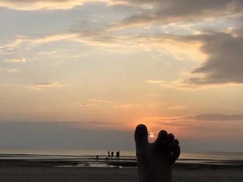 Silhouette hand by sea against sky during sunset